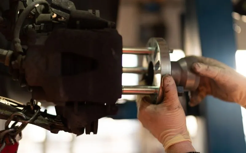 A mechanic wearing protective gloves installs a metal component onto a vehicle's wheel hub assembly in a professional repair shop