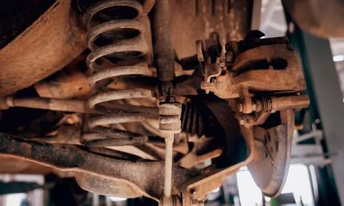 Detailed view of rusted car suspension parts including coil springs and brake calipers under a vehicle