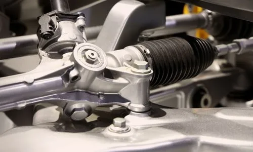 Close-up of a modern steering rack and pinion assembly featuring a black rubber bellows boot and silver metal housing in a vehicle chassis
